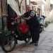  un uomo di bassa statura e grossa corporatura ed  vestito con scarpe anti infortunio scure, jeans, maglione a righe, gilet con tasche e un borsello di pelle scura, l dove ripone i suoi guadagni